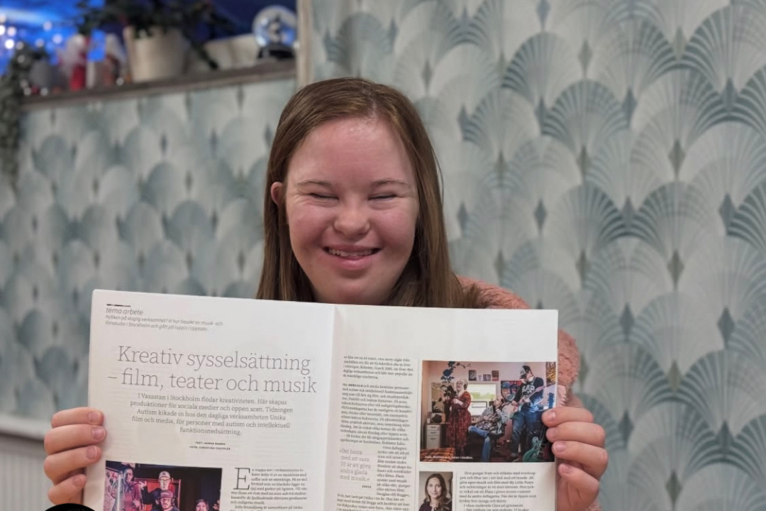 En av deltagarna på daglig verksamhet håller upp tidningsuppslaget och ler.